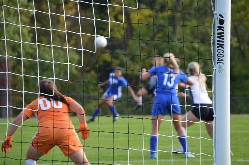 Women's Soccer player kicking the ball into the goal.
